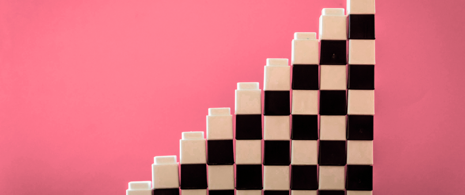 Stacked black and white checkered blocks form a staircase shape against a pink background, creating a striking and modern geometric design.