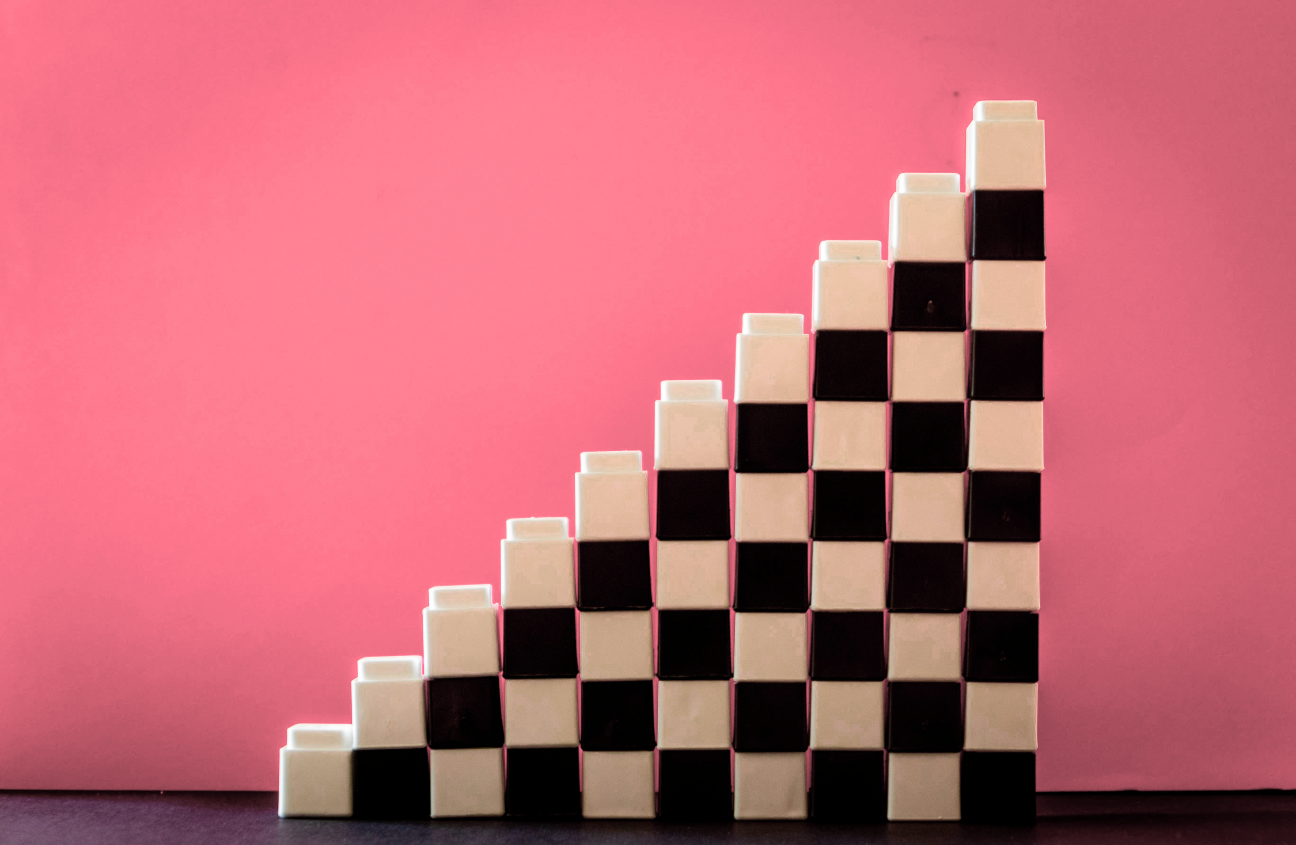 Stacked black and white checkered blocks form a staircase shape against a pink background, creating a striking and modern geometric design.